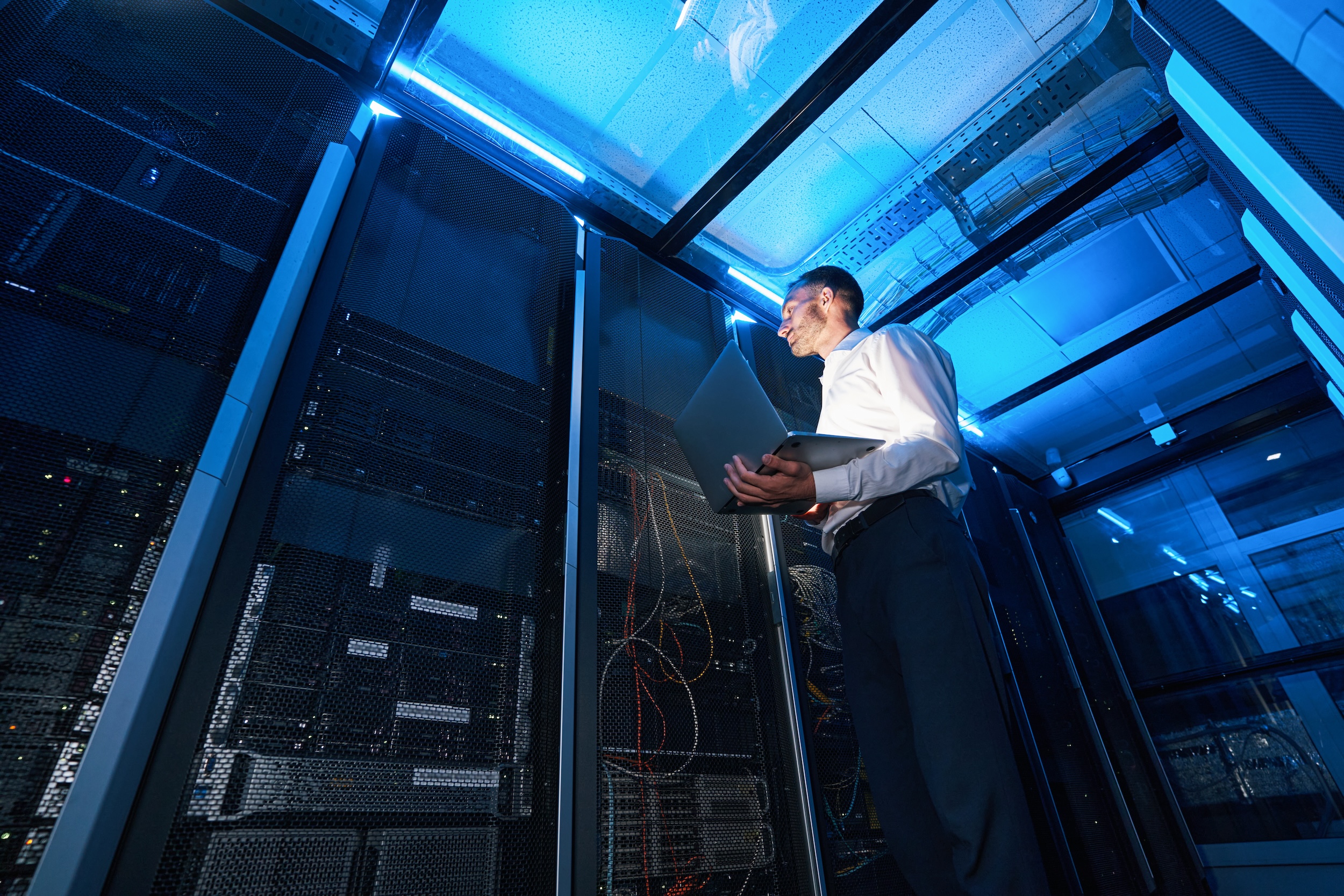 Server administrator of data center with laptop in one hand checking network cabinet