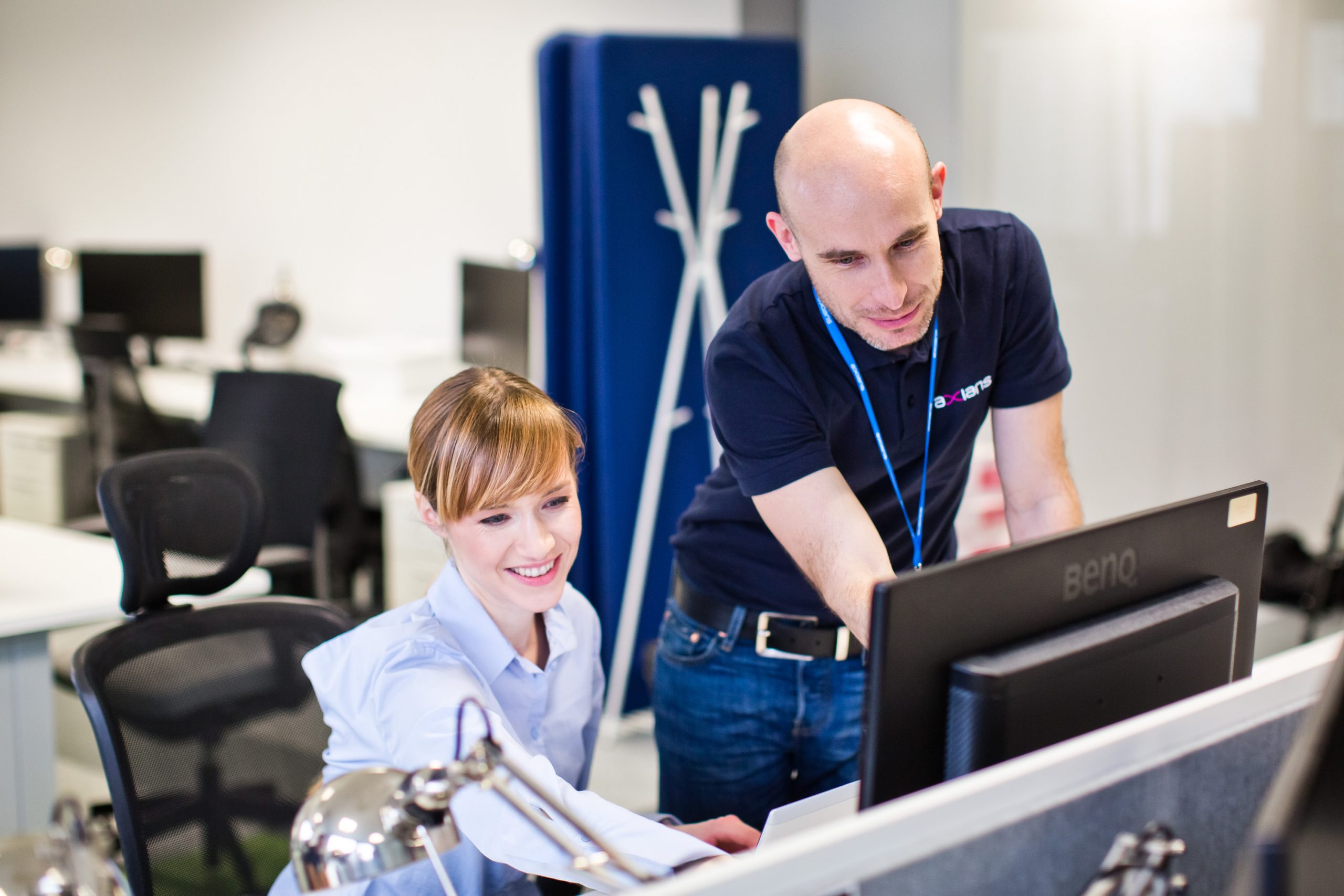 Två arbetskollegor som samarbetar och jobbar tillsammans framför en datorskärm.